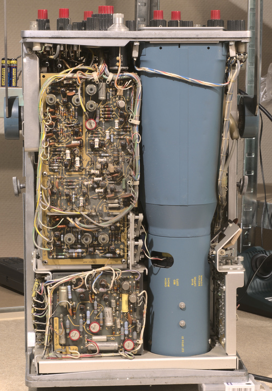 Top side view of the Tektronix type 453 analog oscilloscope with the top and bottom cover removed showing very tightly packed internal circuitry next to the CRT mylar casing that extends across the full depth of the device. 